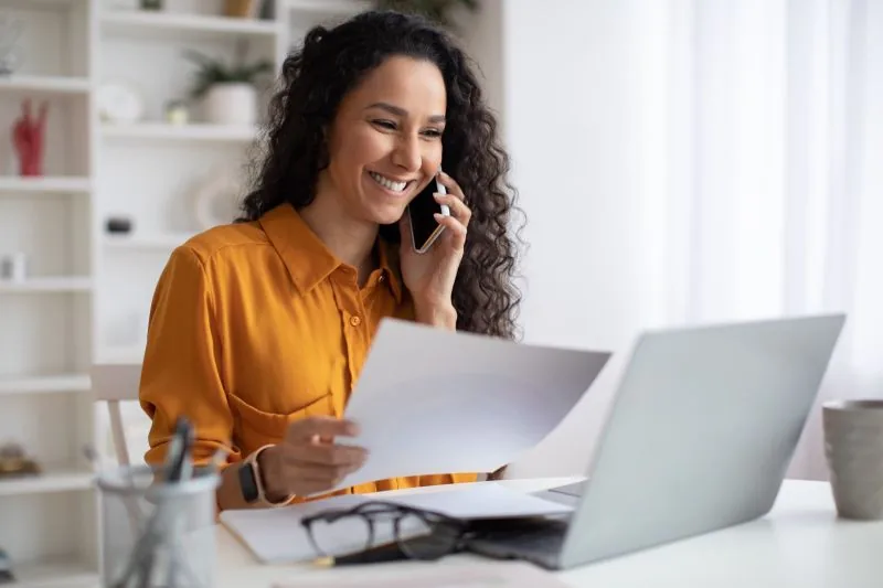Empresária conversa por telefone com a contabilidade enquanto confere documentos da folha. Conteúdo da TCE Contabilidade, contabilidade em Piracicaba/SP.