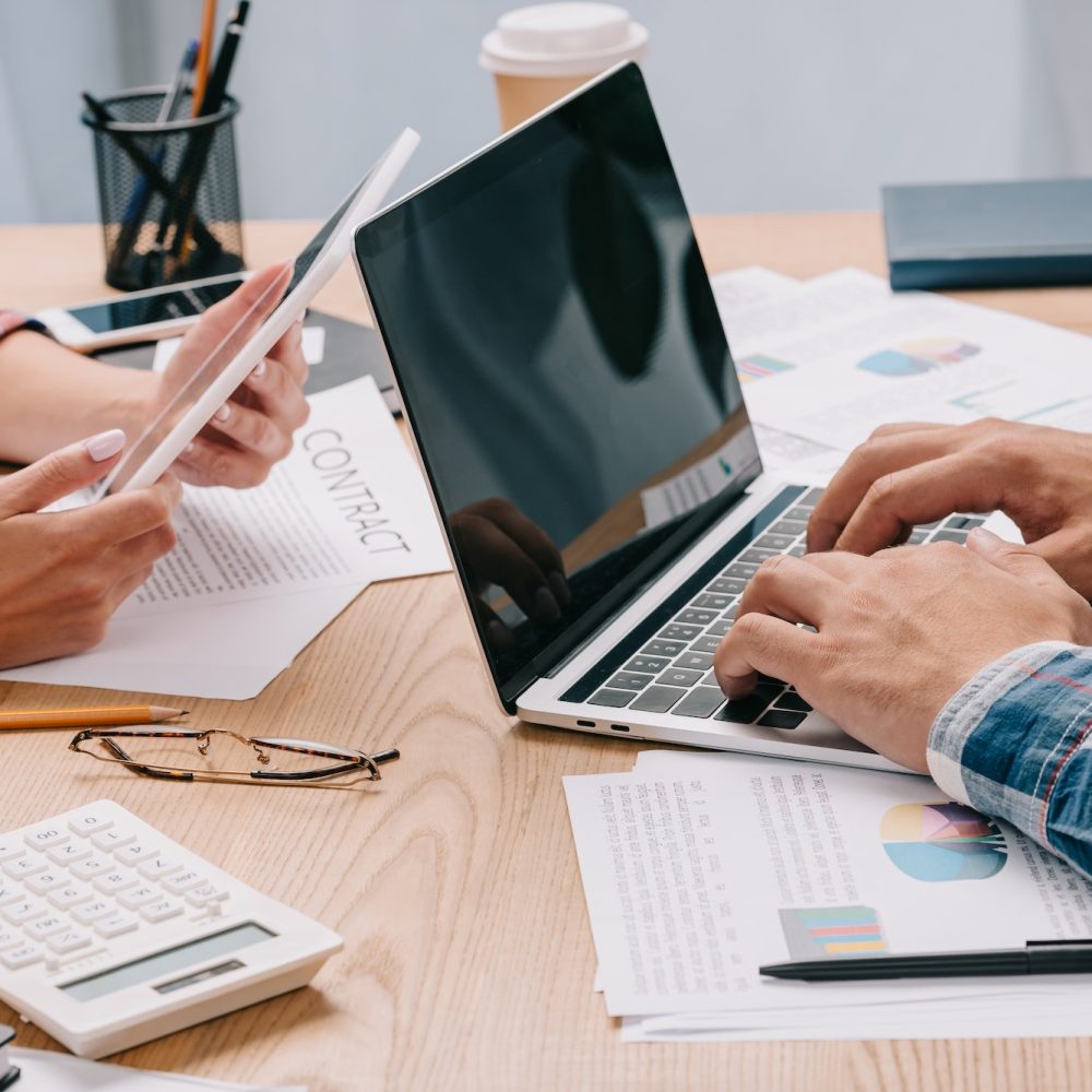 partial view of businesspeople with digital devices working at workplace with papers