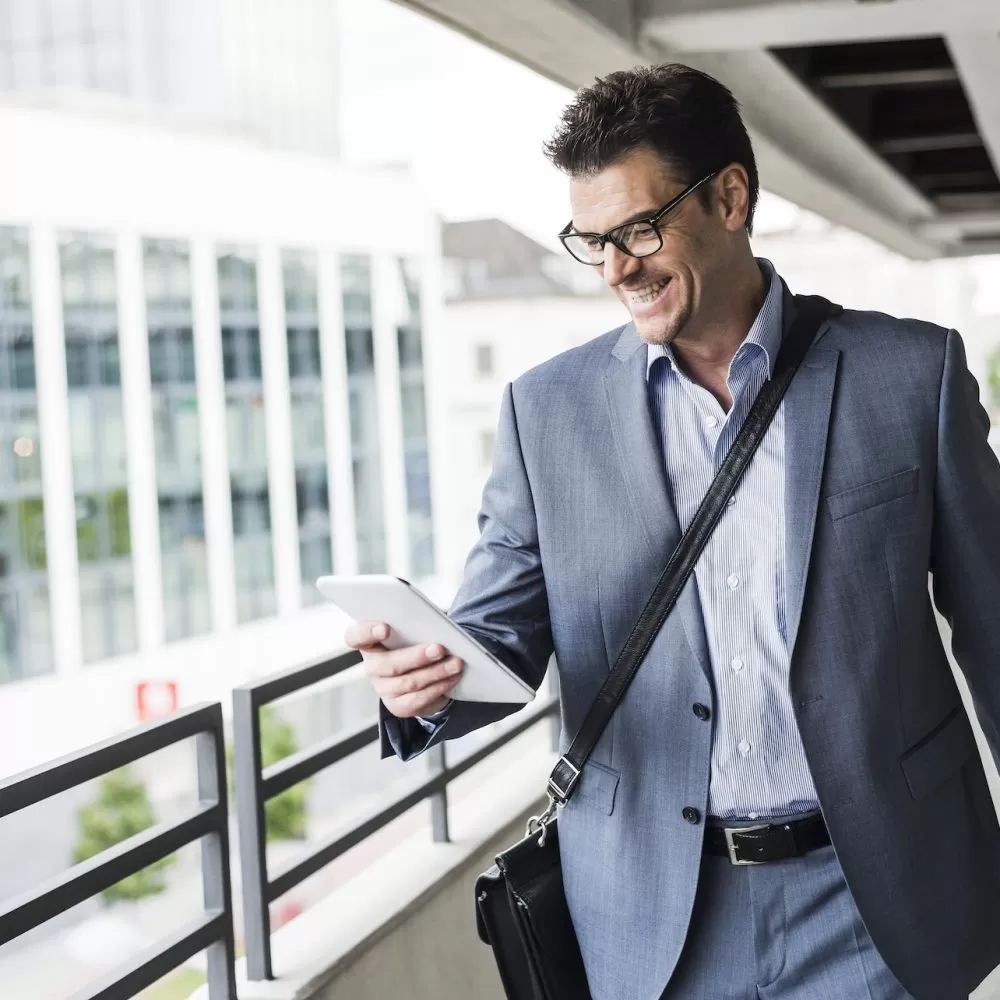 Happy businessman on business trip looking at his mini tablet